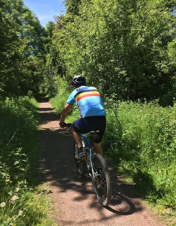 A member of 605 Squadron RAF Reserves passes through a scenic trail on his bike, surrounded by grass and trees as part of the challenge