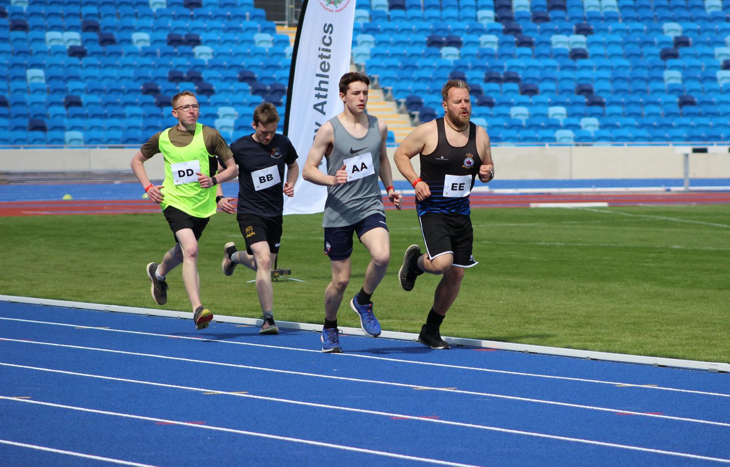 Individual team members from the Army are running along a blue running track as a tight-knit group to compete for the winning places on one of the long distance running track events at the Midlands Army Athletics Championships.