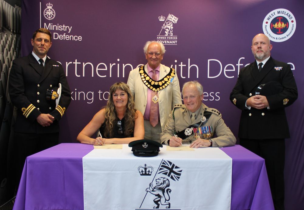 HMS Automated Gates sign the Armed Forces Covenant, seated at a table alongside Colonel Taylor, the Mayor and representatives from BURNU