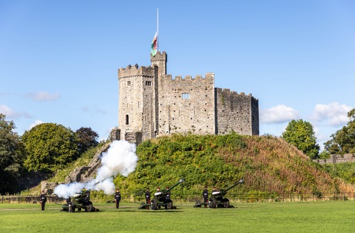 Three large guns are positioned in a row outside of Cardiff Castle. One gun has been fired and smoke is pouring out of the end of the gun.