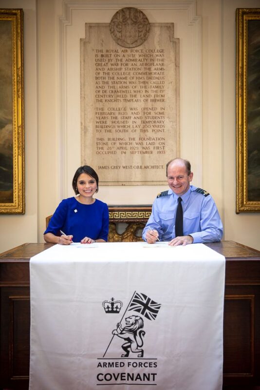 Head of the RAF, Air Chief Marshal Sir Mike Wigston, today supported youth charity the Jon Egging Trust (JET) in its signing of the Armed Forces Covenant at a ceremony at RAF College Cranwell in Lincolnshire. Both Dr Emma Egging and Air Chief Marshal Sir Mike Wigston are pictured sitting at a table with a cloth displaying the Armed Forces Covenant logo, smiling at the camera as they sign the covenant.