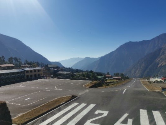 The tarmac runway at Lukla Airport perched in the side of a mountain, with blue skies and other mountains in the distance
