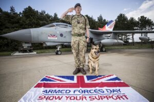 RAf personnel with dog and Armed Forces Day flag in front of a military jet.