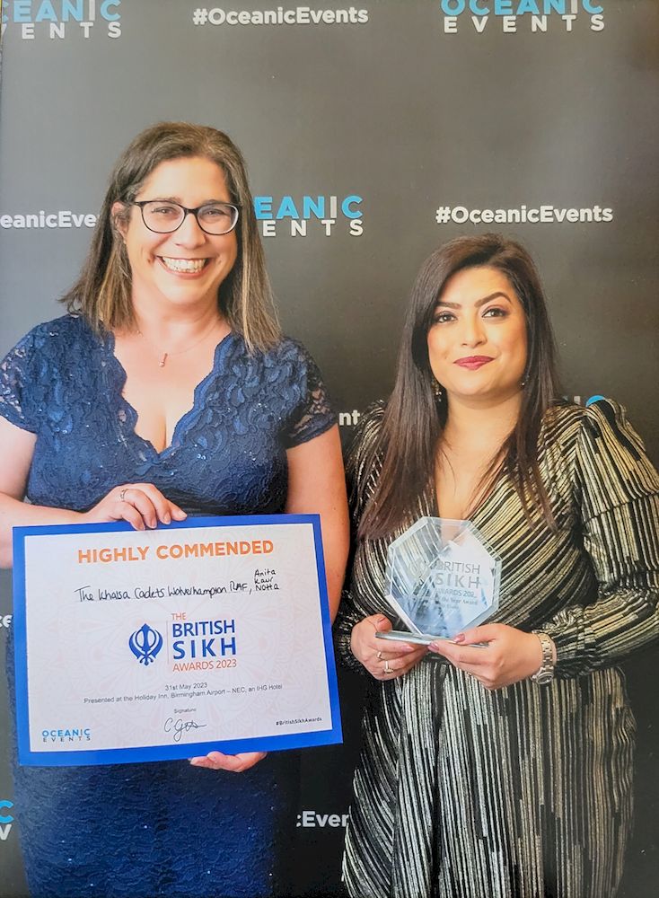 Acting Pilot Officer Charlotte Harding (Contingent Commander) and Anita Notta (Executive Principal of The Khalsa Academies Trust) receiving the Accolade of Highly Commended Award for Community Initiative of the year. They are dressed in formal wear, standing together smiling with their certificate and award.