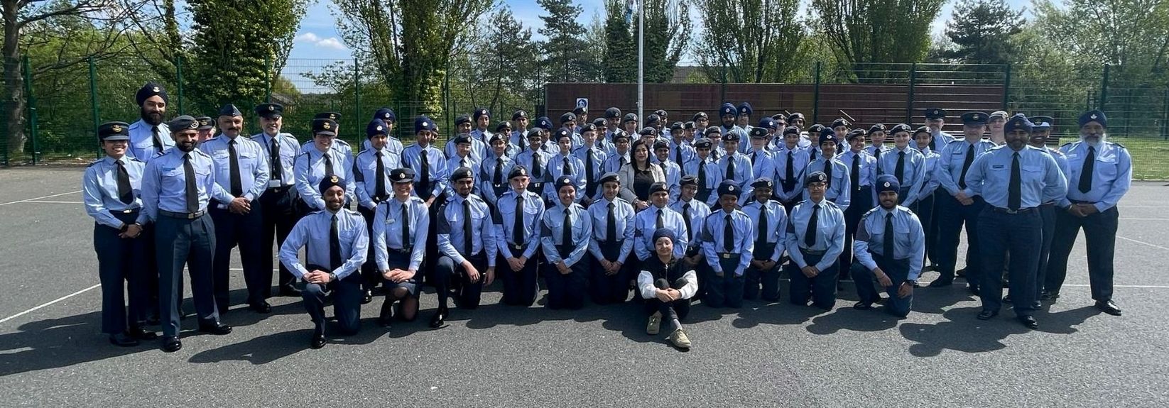 A large group of Royal Air Force Cadets from the Khalsa Academy Wolverhampton are standing outside in their uniforms, smiling at the camera. They are in two rows, with the front row crouching on one knee.