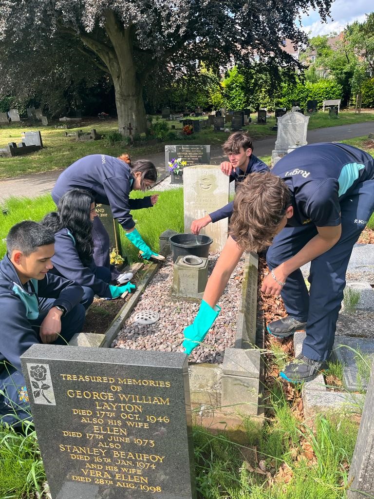 A group of cadets are cleaning and tidying a WW2 grave and headstone.