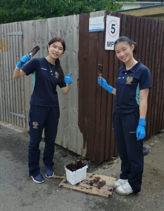 Two cadets are painting a brown fence