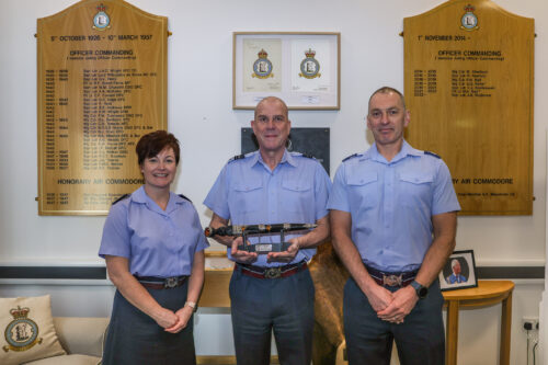 Three members of 605 Squadron are smiling and holding the Kemp Dirk Trophy, won by the squadron. 