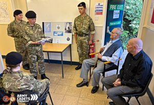 An Army Cadet from the Worcester Troop is reading from a piece of paper, sharing their presentation prepared especially for Ken. Ken and his son are sitting listening intently amongst the the rest of their Army Cadet Troops.